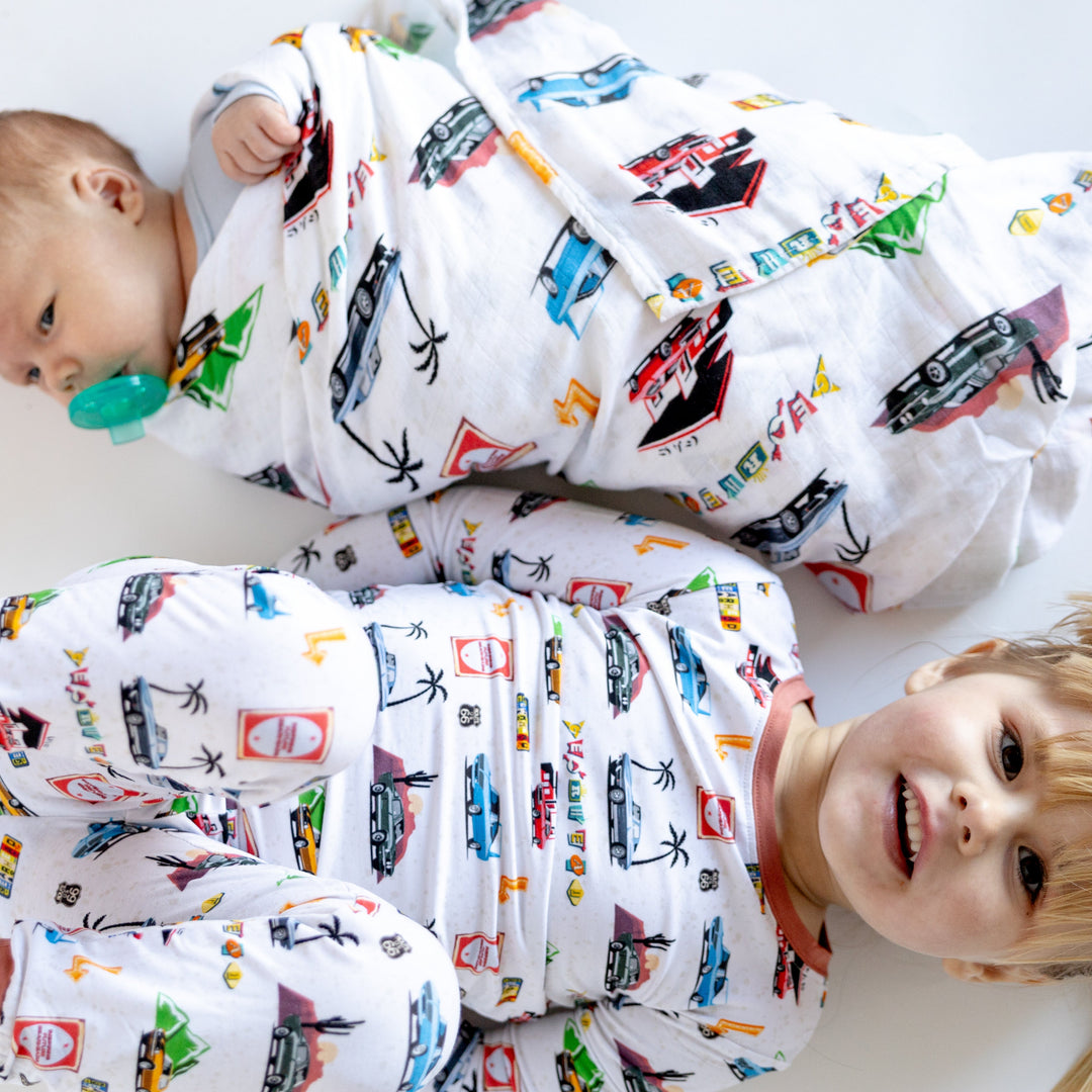 Infant wrapped in the American Road Trip Muslin blanket and a little girl wearing matching pajamas featuring Corvette, Camaro, Superbird and other muscle cars - Gearhead Kids 
