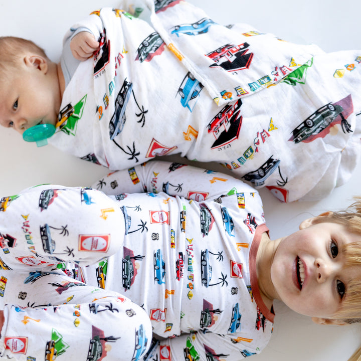 Infant wrapped in the American Road Trip Muslin blanket and a little girl wearing matching pajamas featuring Corvette, Camaro, Superbird and other muscle cars - Gearhead Kids 