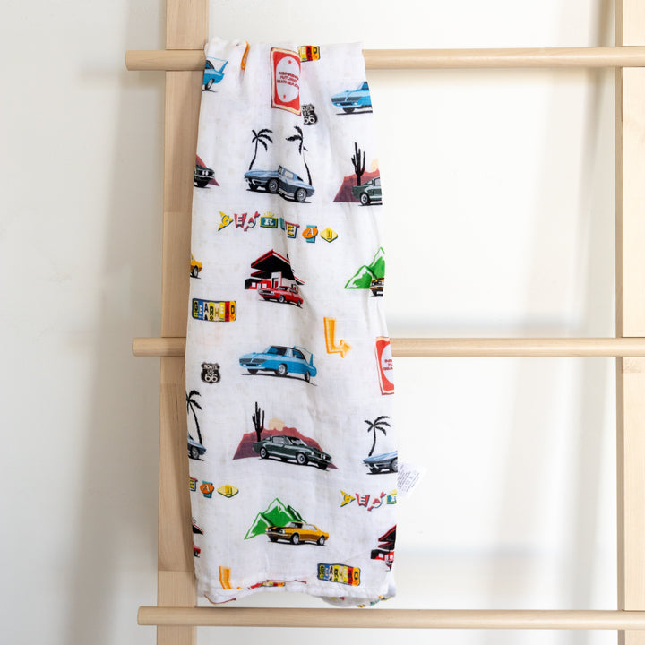 A muslin bamboo swaddle blanket with a pattern of classic american muscle cars displayed on a wooden ladder.