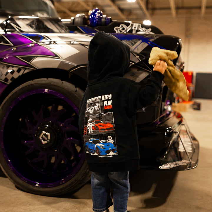 Little boy wearing a Gearhead Kids American Muscle Play Garage Hoodie featuring a white Ford GT, Red Corvette ZR1 and a Dodge Viper ACR