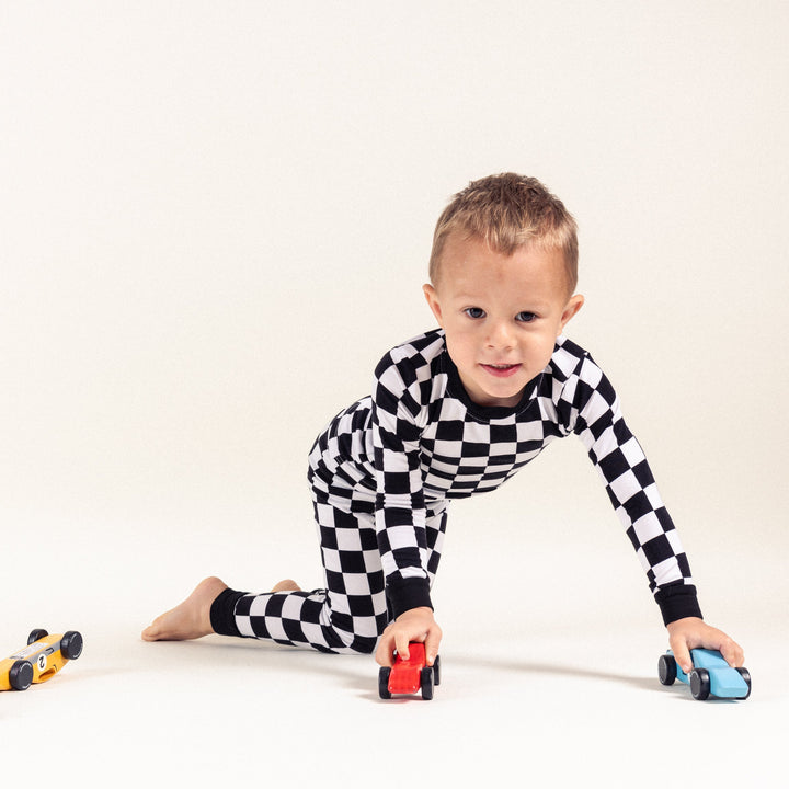 Little boy in black and white bamboo checkered pajamas playing with cars - Gearhead Kids