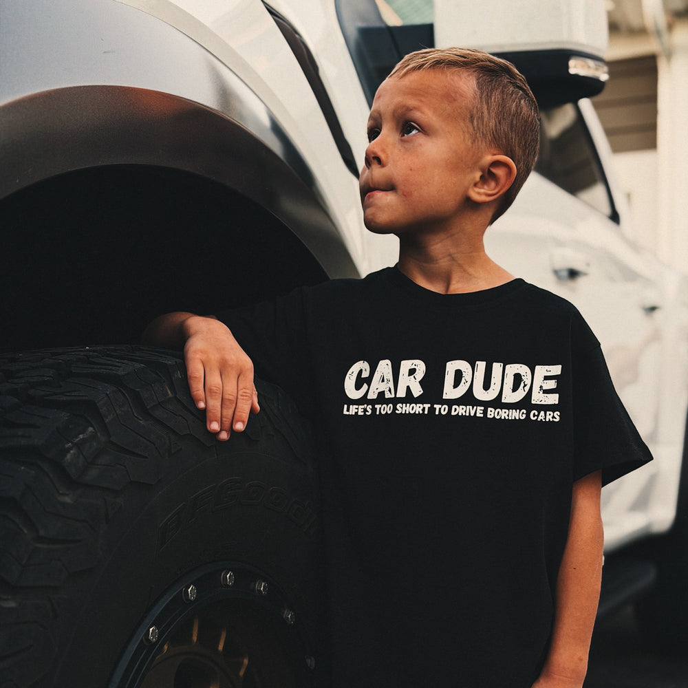 young kid wearing a black t-shirt with white text "CAR DUDE"  "Life's too short to drive boring cars" by Gearhead Kids