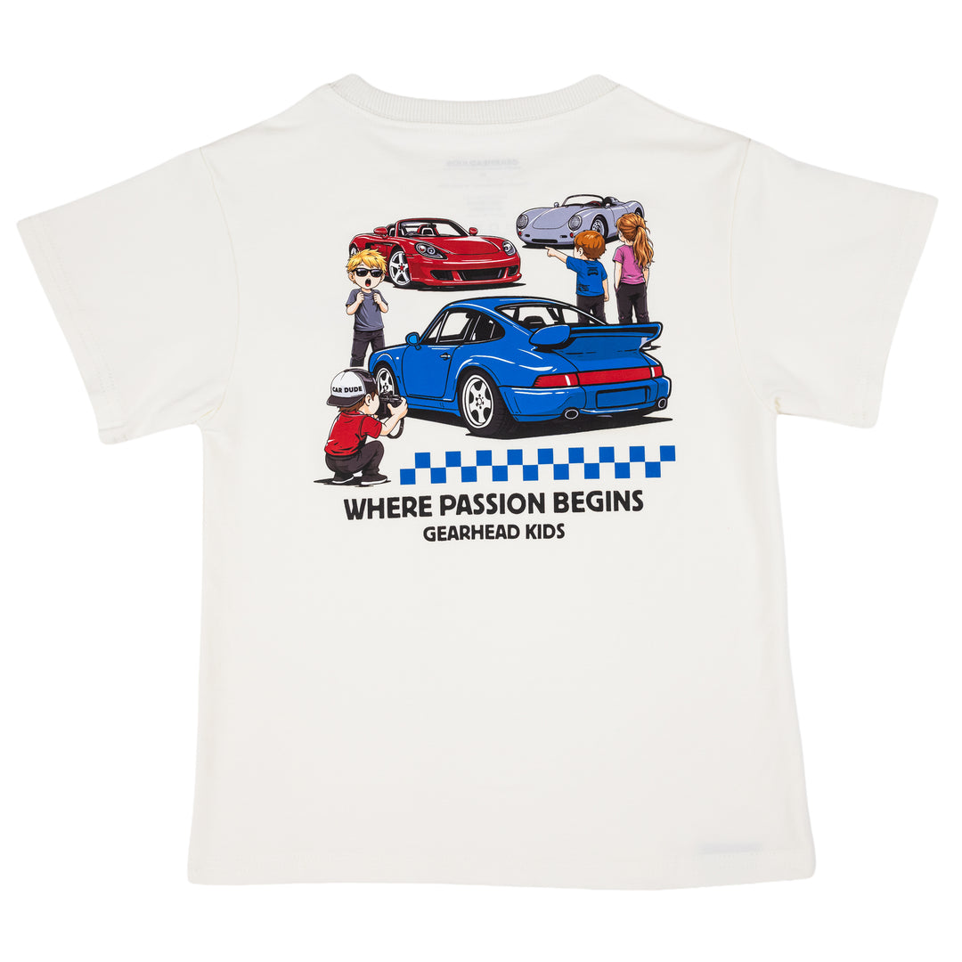 Off-white short-sleeve t-shirt featuring a 964 turbo sports car, silver 550 spyder and a red mid-engine supercar, with the text 'WHERE PASSION BEGINS GEARHEAD KIDS' printed below.