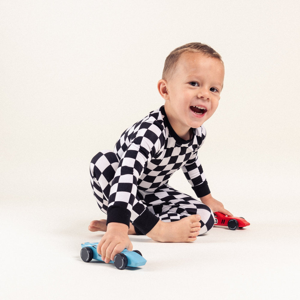 Boy in bamboo black and white checkered pajamas playing with wooden cars - Gearhead Kids