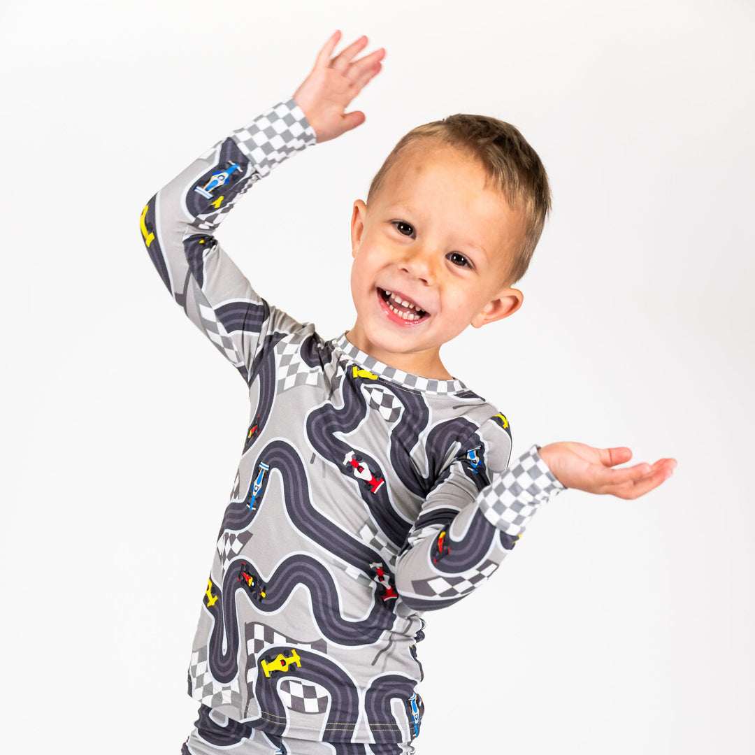 Boy wearing Circuit Dreamer baby pajamas with open-wheel F1 and Indy style race cars on a track - Gearhead Kids