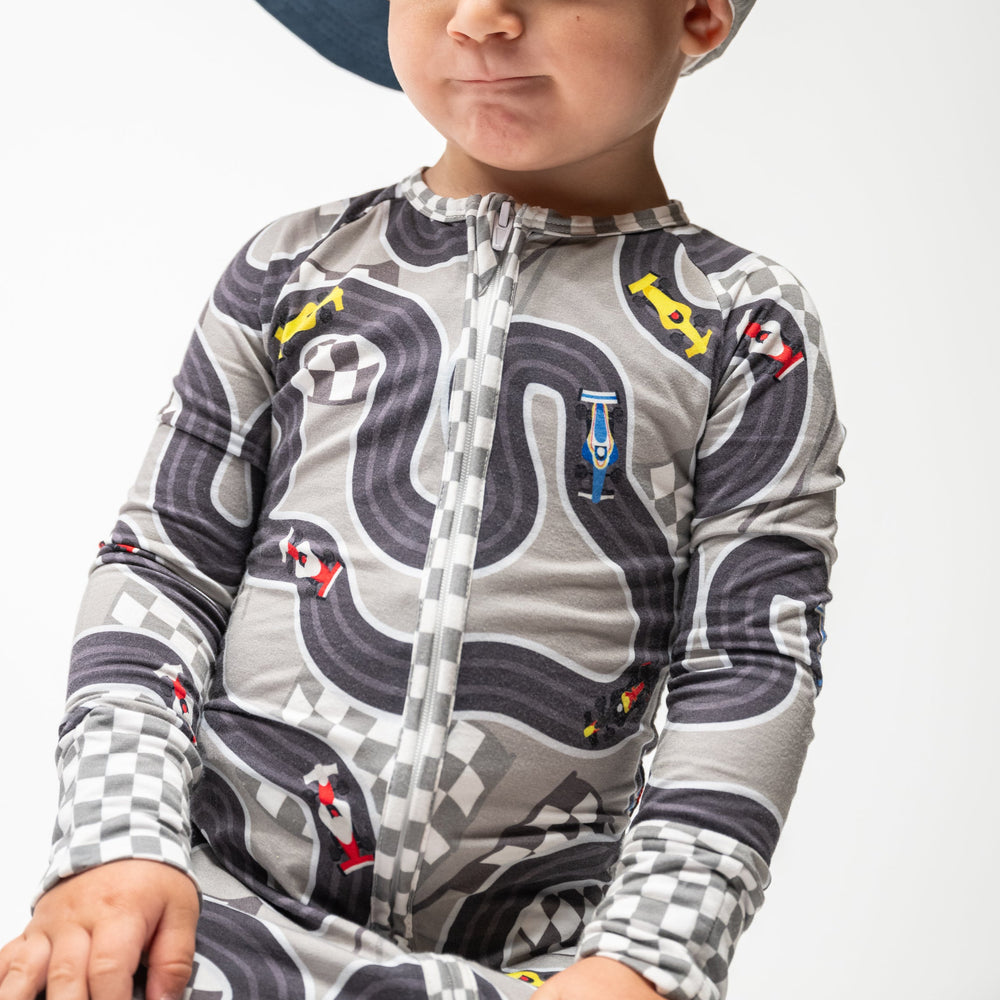 A child wearing long-sleeved pajamas with a race track and cars pattern, featuring a full zipper, fold-over feet, and mittens - Gearhead Kids