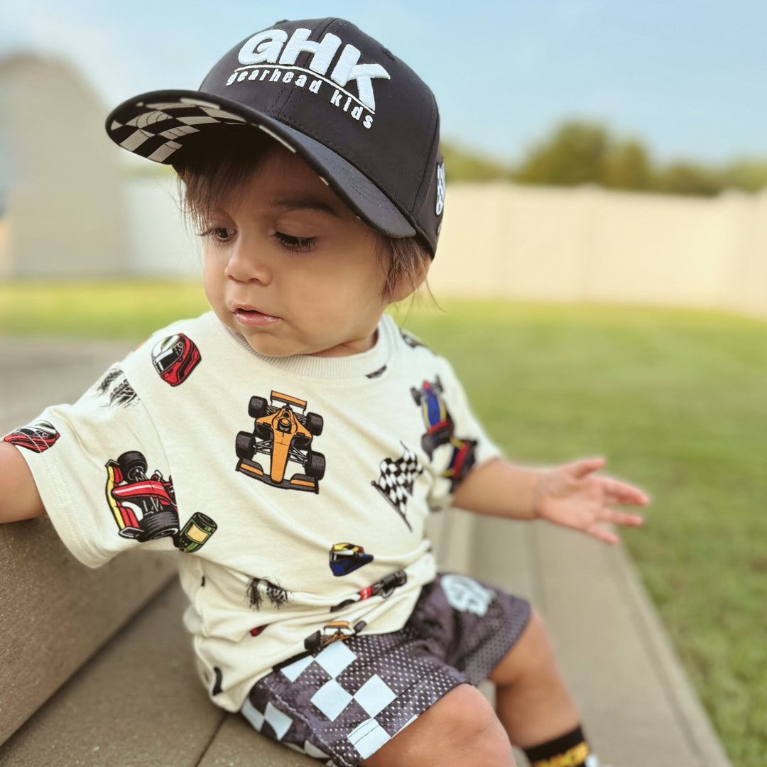 Little boy wearing a grand prix themed t-shirt featuring Formula 1 race cars, flags, champagne bottles and race helmets.  | Gearhead Kids
