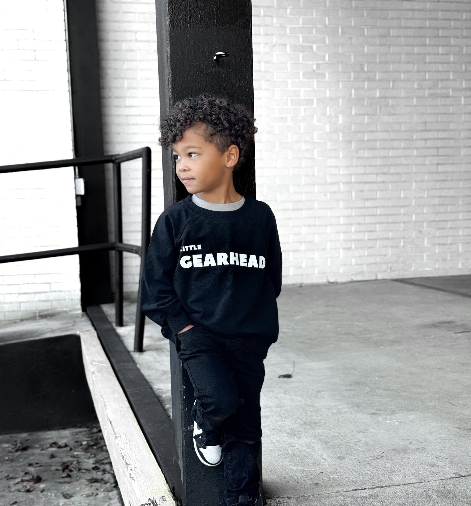 Boy wearing a black sweatshirt with LITTLE GEARHEAD white letters - Gearhead Kids