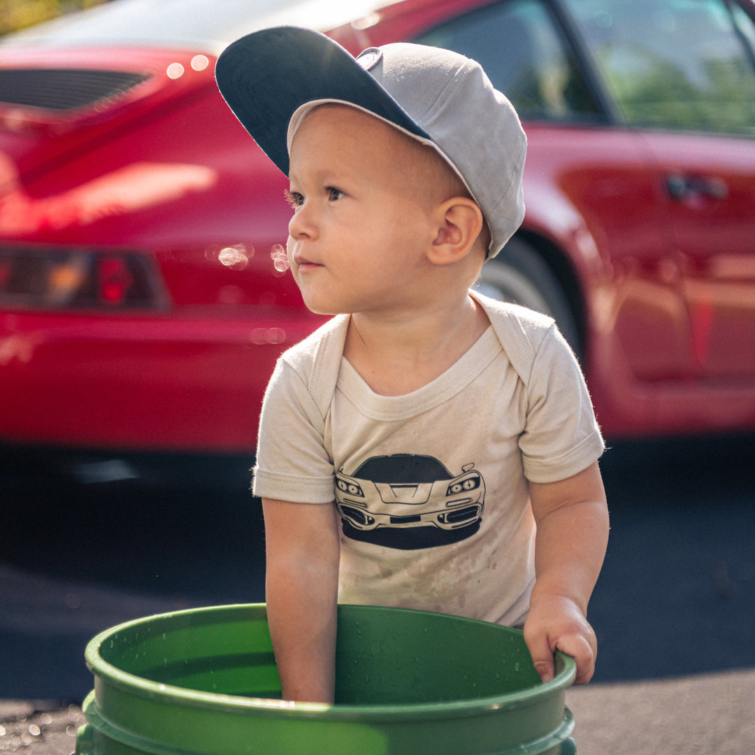 Toddler boy wearing McLaren F1 onesie and washing a car