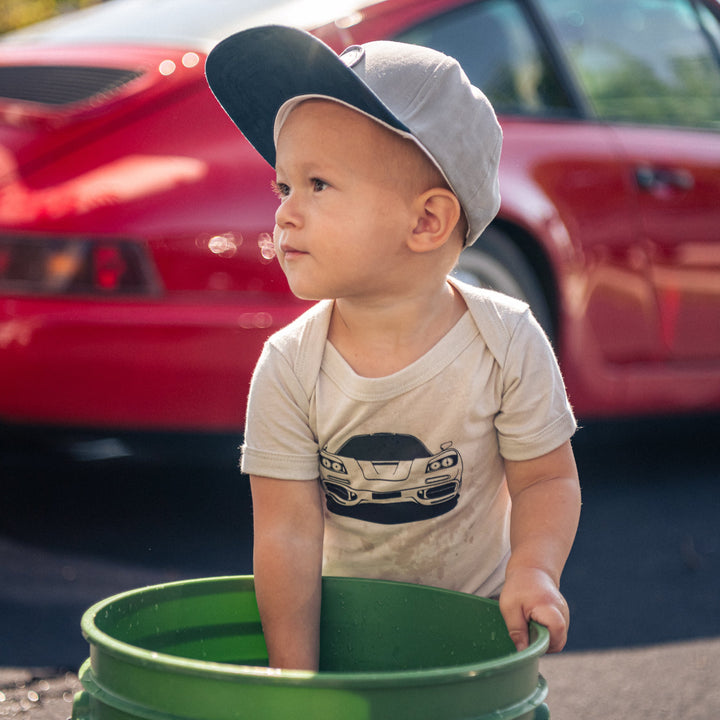 Toddler boy wearing McLaren F1 onesie and washing a car