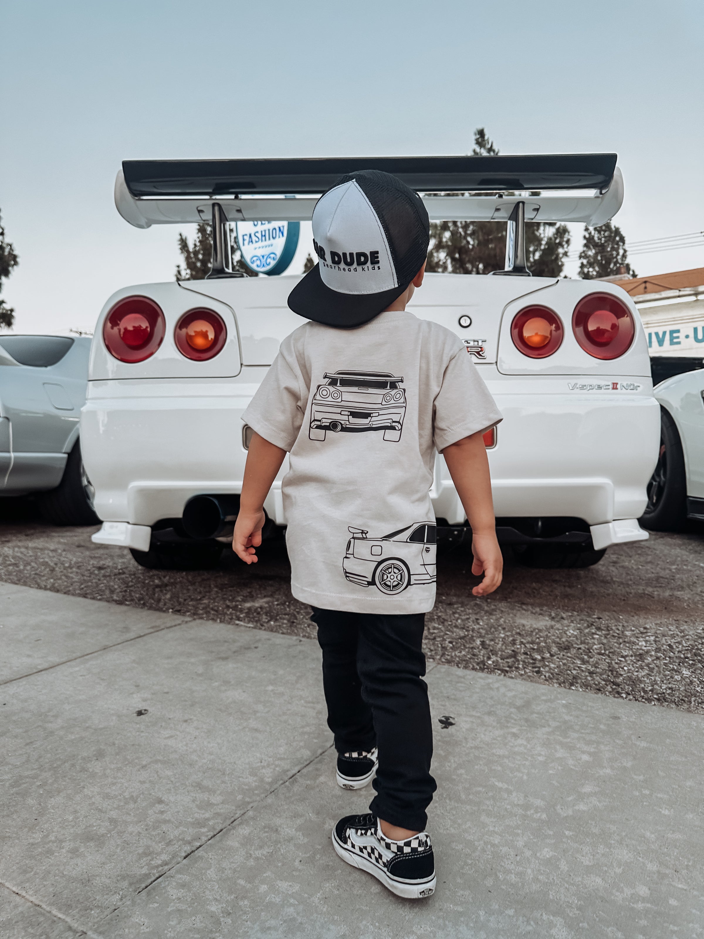 little boy wearing a GTR R34 t-shirt and a CAR DUDE hat looking at the back of a Nissan GTR - Gearhead Kids