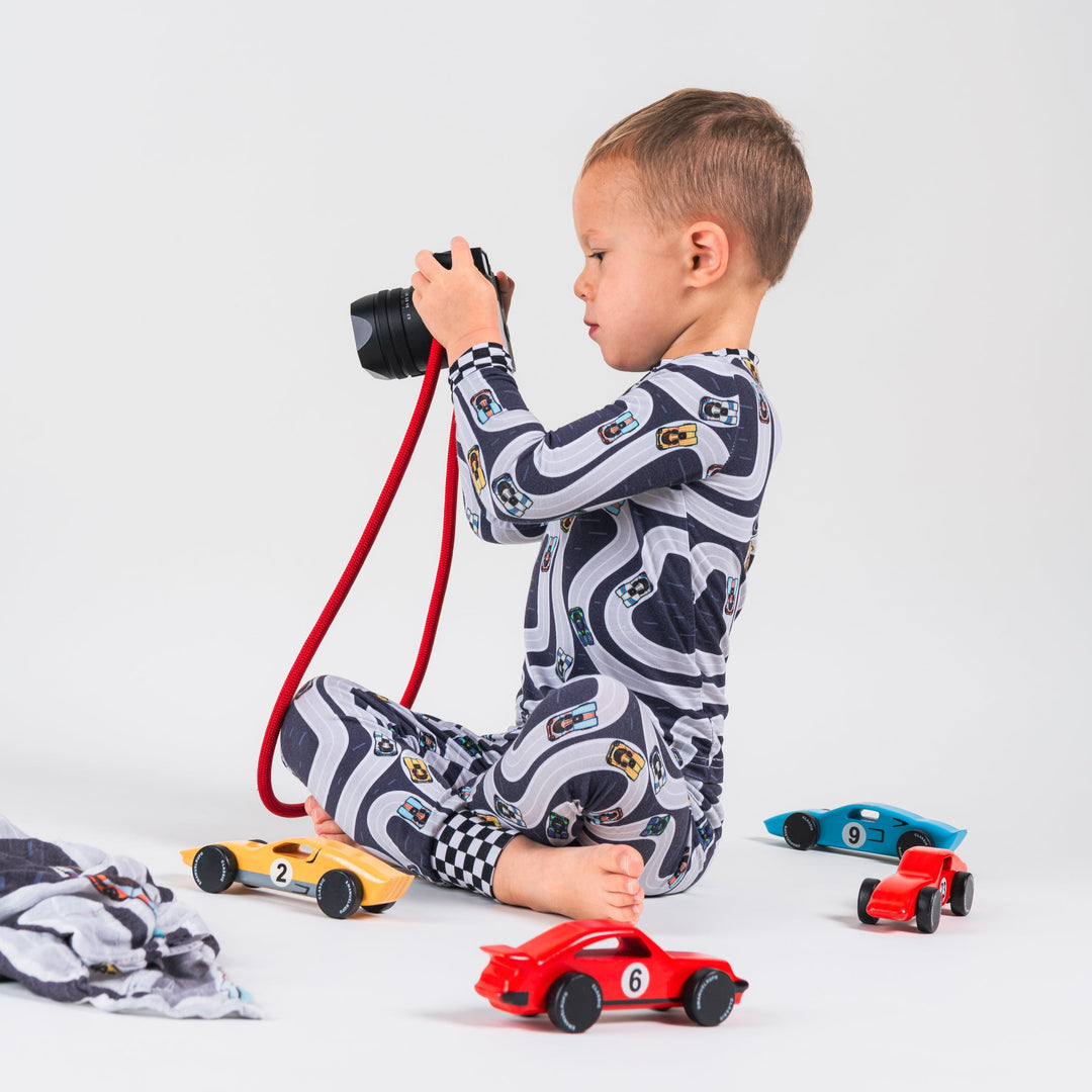 Little boy surrounded by wooden cars wearing bamboo pajamas featuring Porsche 917 in classic liveries on a race track - Car photographer - Gearhead Kids