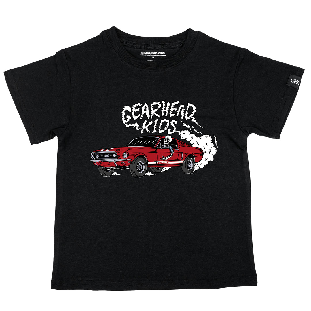 Kids black t-shirt featuring a skeleton driving a red classic GT500 fastback Mustang doing a burnout with Gearhead Kids smoke graphic