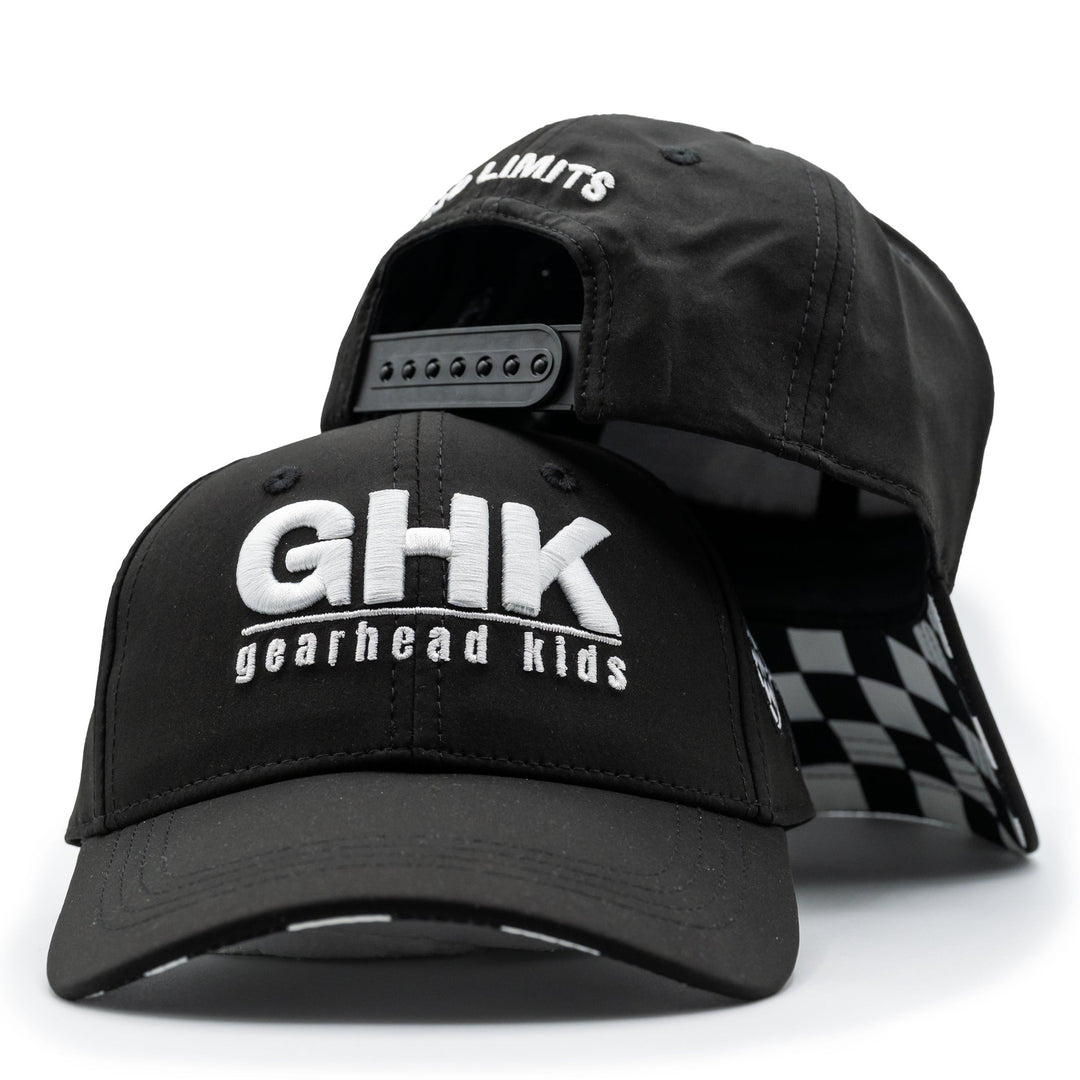 A black structured baseball cap with 'GHK gearhead kids' printed in white on the front, shown with a second cap behind it that reveals a black-and-white checkered interior lining and an adjustable back strap.