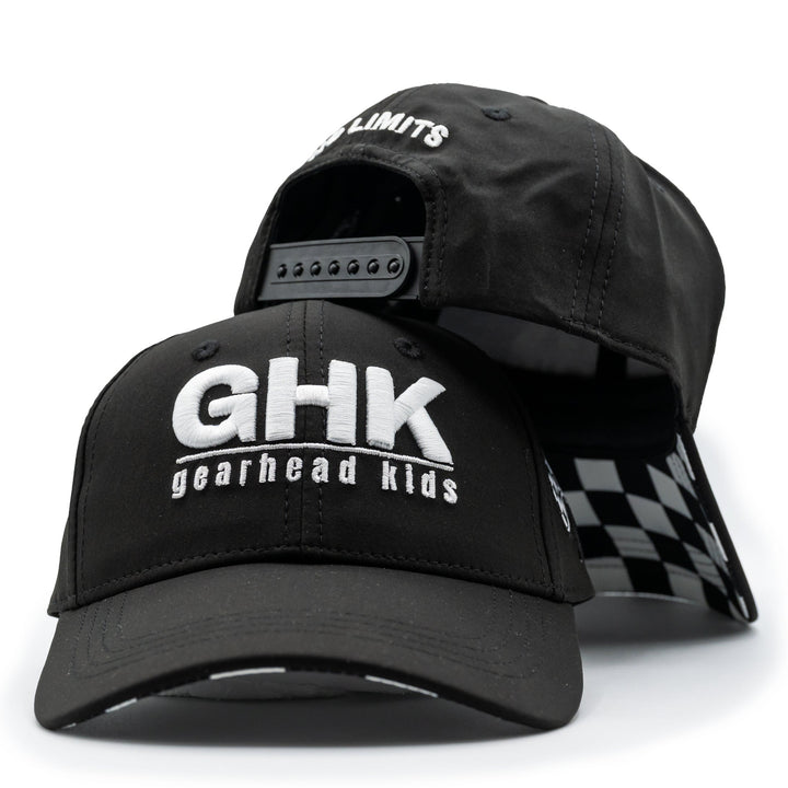 A black structured baseball cap with 'GHK gearhead kids' printed in white on the front, shown with a second cap behind it that reveals a black-and-white checkered interior lining and an adjustable back strap.